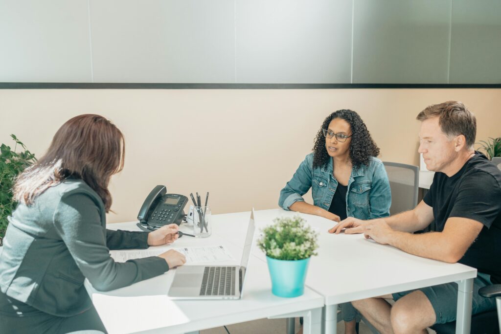 pexels-photo-8301240-8301240 Anonymous female employee interacting with diverse clients at table with netbook and paper sheet in workspace